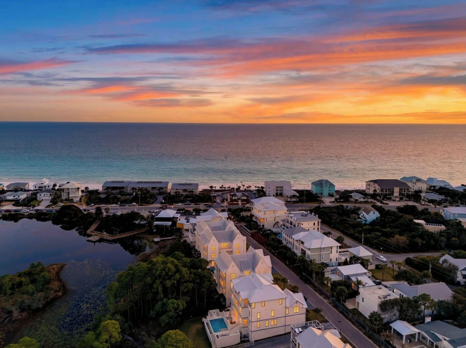 Sunset casting a warm glow over waterfront homes, with the ocean stretching out beneath a painted sky.