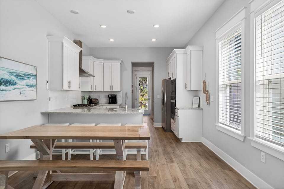 Open‑concept coastal dining area with natural wood tones, soft beachy hues, and sunlight flowing through the home.