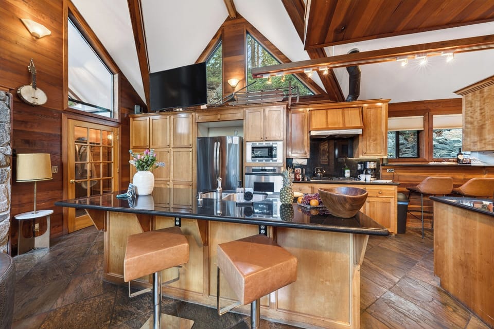 Warm, wood‑toned kitchen with a spacious island, modern appliances, and vaulted cabin windows bringing in the forest light.