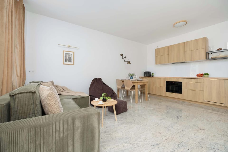 A view of the living area combined with the dining room, featuring a stylish wooden table with chairs. In the background, a sofa and a window with delicate curtains are visible.