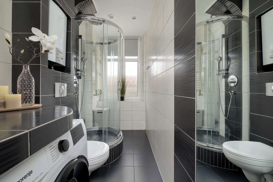 A detailed view of the bathroom shows the glass shower enclosure and the modern vanity with a large mirror above it. Potted candles and decor on the ledges create a spa-like feel.