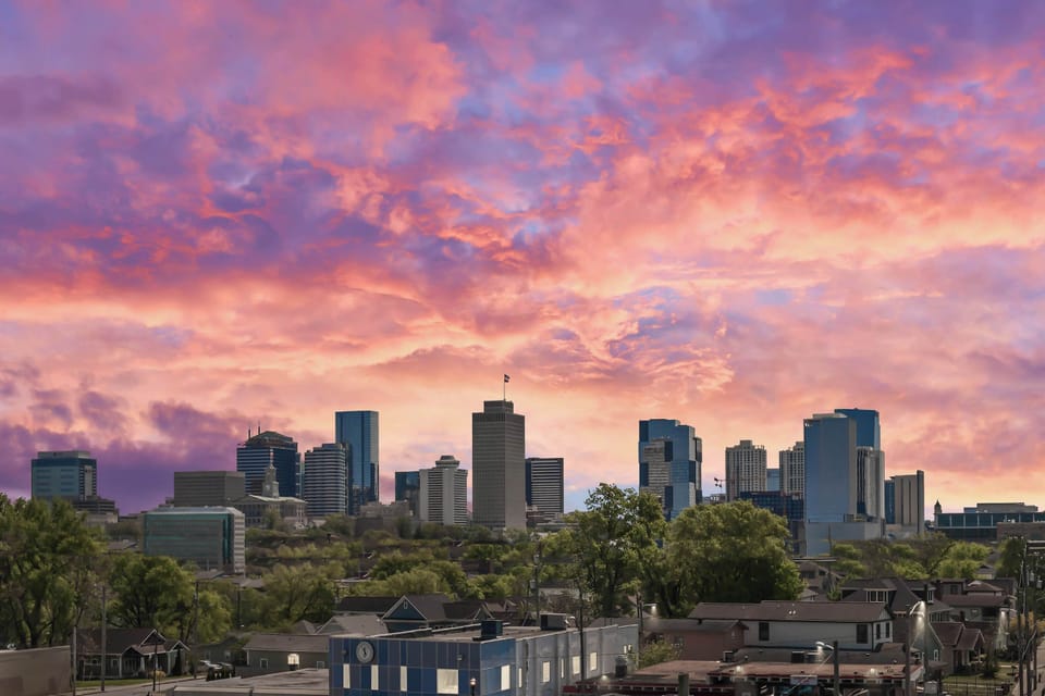 Unobstructed panoramic views of the downtown Nashville skyline—visible from every corner of the terrace under a dramatic pink and purple Nashville sunset and skyline as the backdrop.