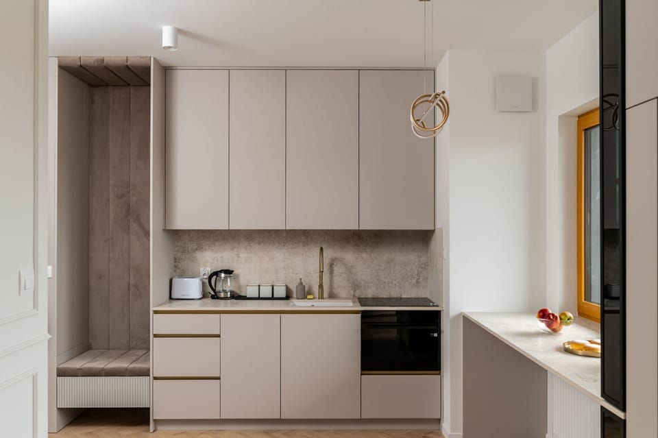 A modern kitchenette in muted beige tones with floor-to-ceiling cabinets. The minimalist design is accentuated by subtle handles and built-in appliances.