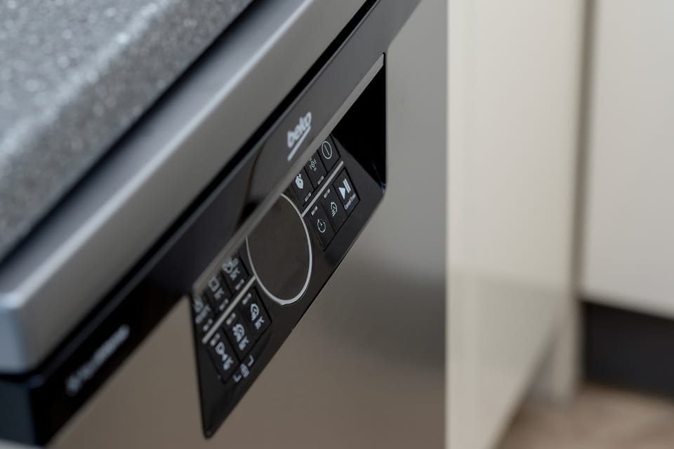 The sleek interface of a black dishwasher or oven is shown in a tight detail shot. The glossy finish and digital icons suggest high-end, contemporary kitchen equipment.