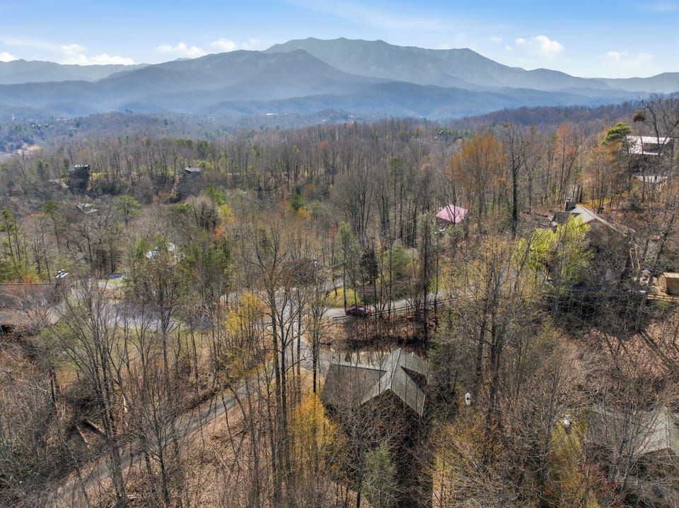 Aerial view showcasing the property nestled among wooded hills with stunning mountain vistas and peaceful residential surroundings.