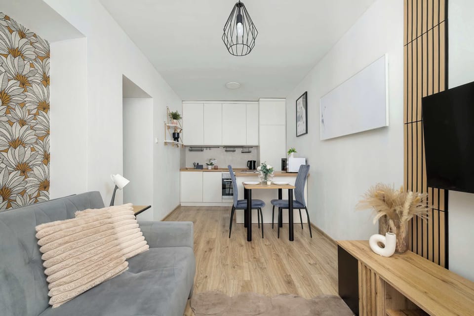 A view into an apartment from the entrance, showcasing a grey sofa, a living area, and the open-plan kitchen and dining space in the background.