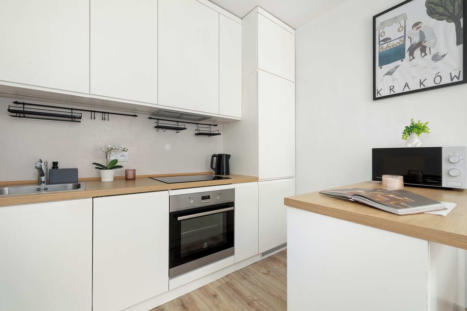 A modern kitchen featuring white, handleless cabinetry and wooden countertops. The built-in oven and black cooktop are the central elements.