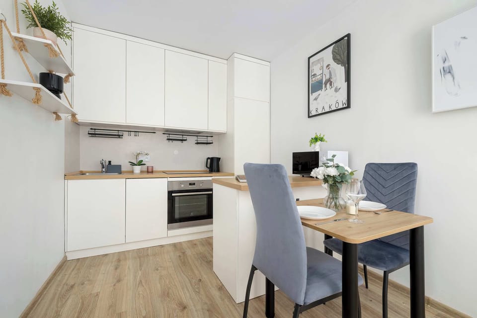 Another angle of the open-plan kitchen and dining area, highlighting the two blue chairs and the light wood table against the white cabinets.