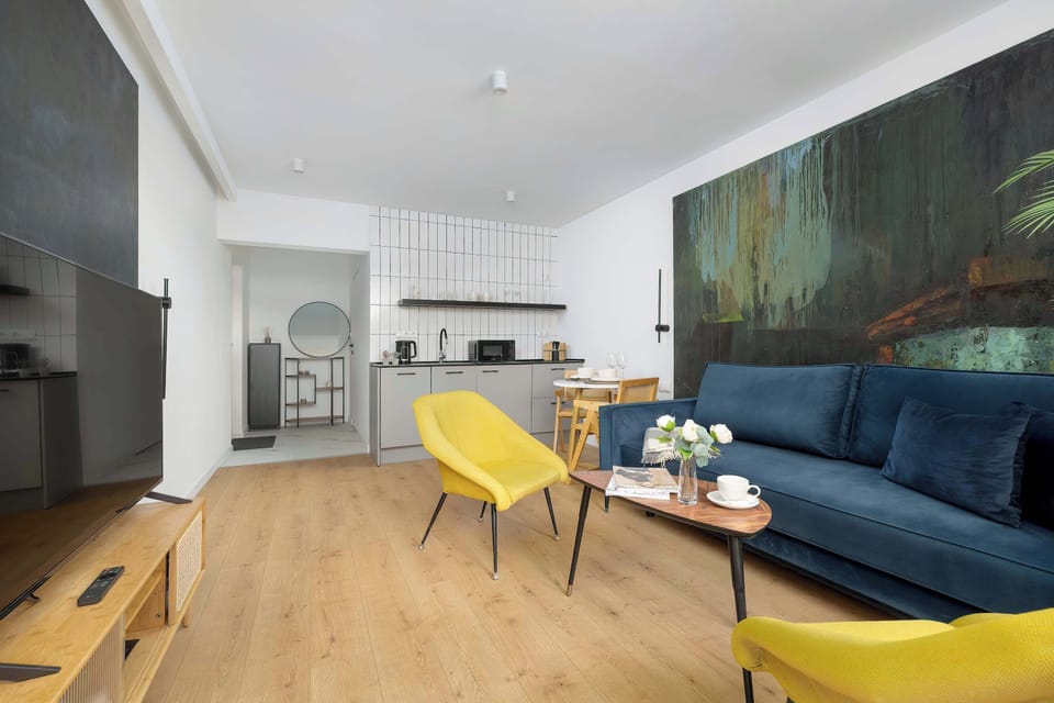 The open-plan layout connects the living area to a small kitchenette in the background. Light wood flooring and bright white walls enhance the sense of space and modern style.