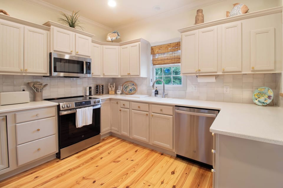 Your fully equipped kitchen features gleaming white cabinets, modern appliances, and warm wood floors—perfect for preparing meals during your stay.