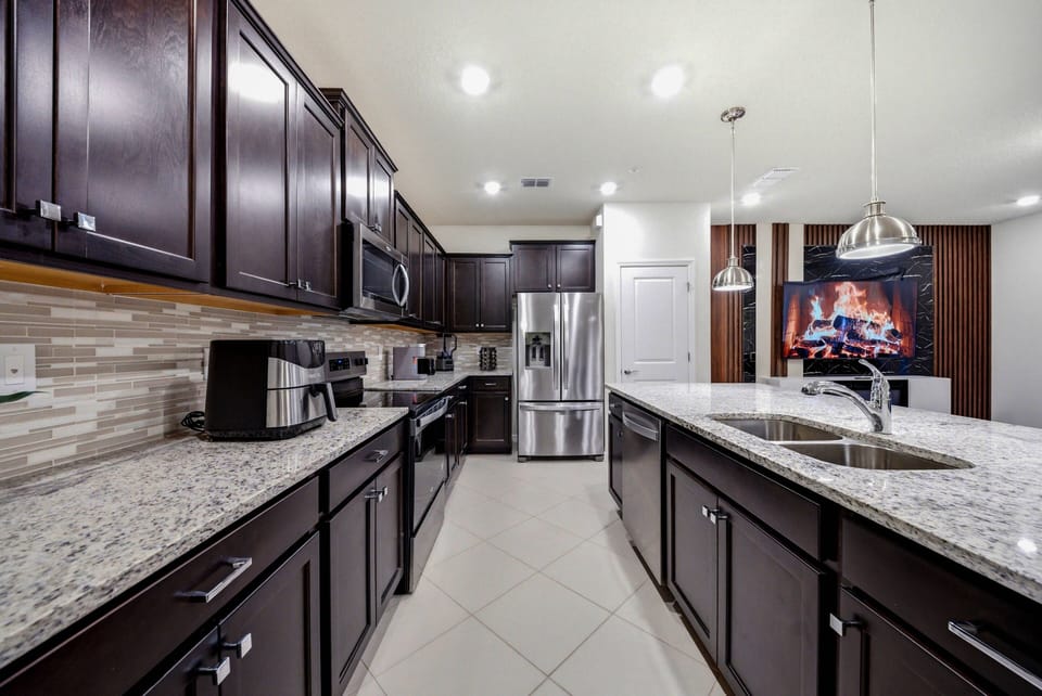 Experience a beautifully designed kitchen with rich dark cabinetry and stunning granite countertops, complemented by sleek stainless steel appliances and modern pendant lighting, perfect for your culinary adventures.