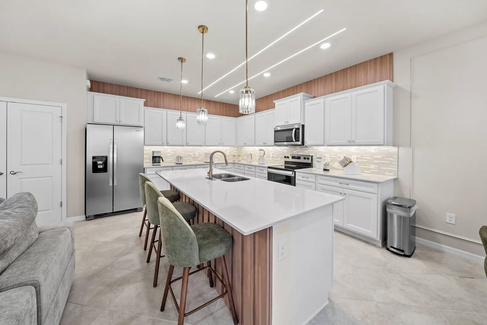Experience a beautifully designed kitchen with sleek white cabinets and warm wood accents. The spacious island, topped with an elegant countertop, is perfect for meals and gatherings under chic pendant lights.