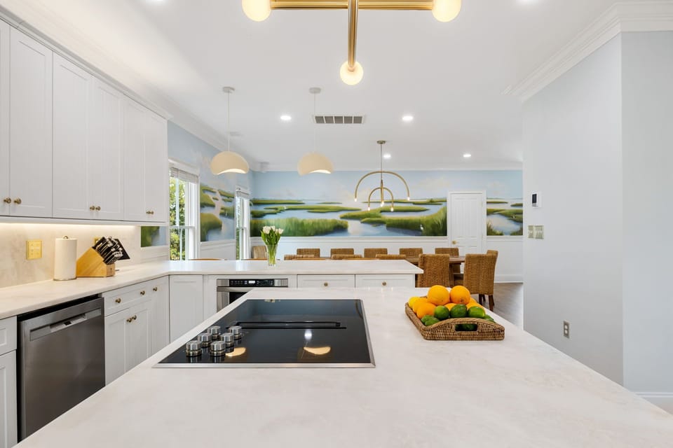 Your stunning open kitchen flows seamlessly into the dining area, featuring pristine white countertops, modern appliances, and warm pendant lighting.