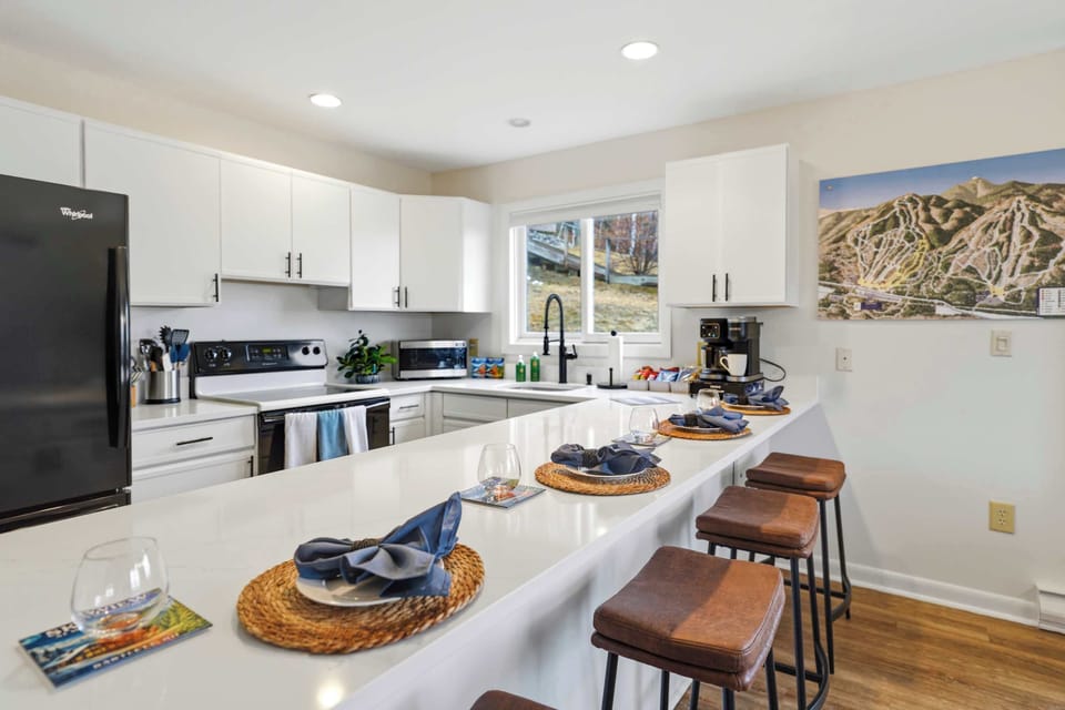 The kitchen island with four leather stools — clean counters, white cabinets, and everything you need already in place.
