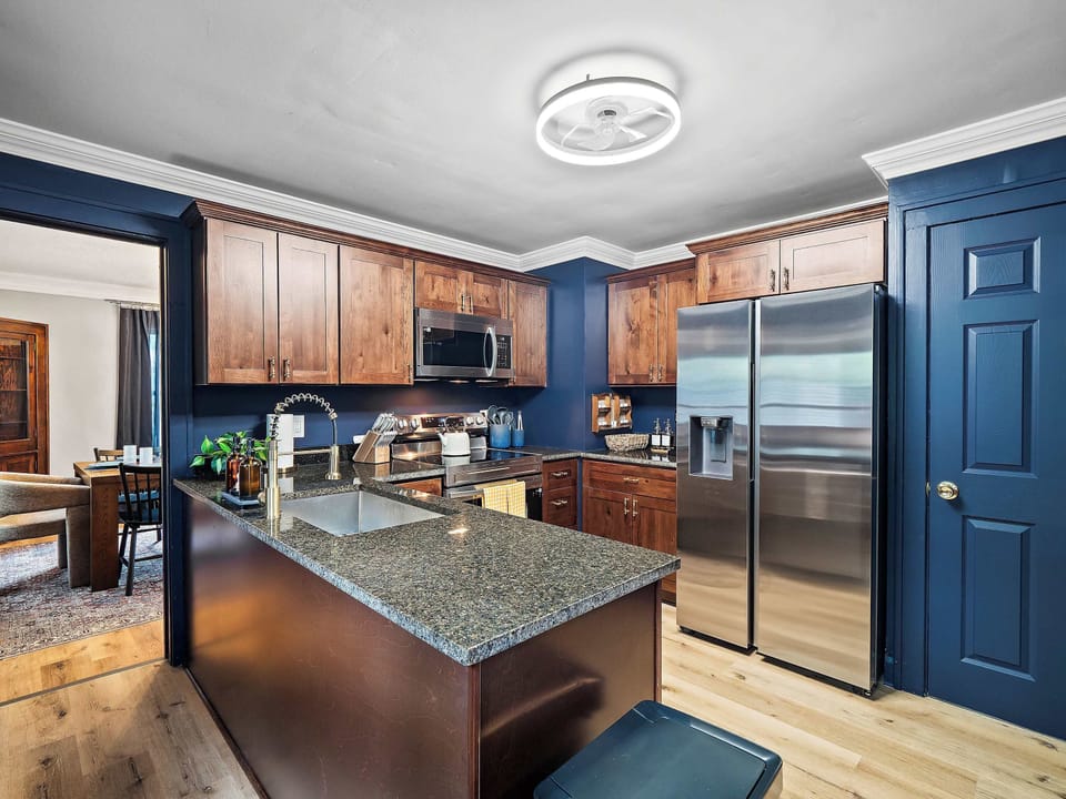 Fully equipped kitchen w/ stainless fridge, island & warm wood & blue tones throughout.
