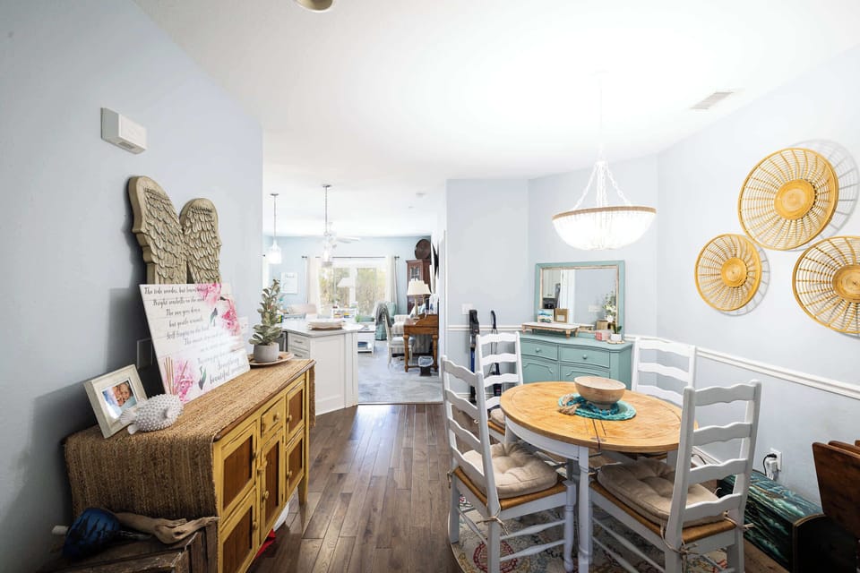 Charming dining area with round table seating with coastal-inspired décor, soft lighting, and a welcoming entryway that flows into the open kitchen and living area for a warm, homey feel.