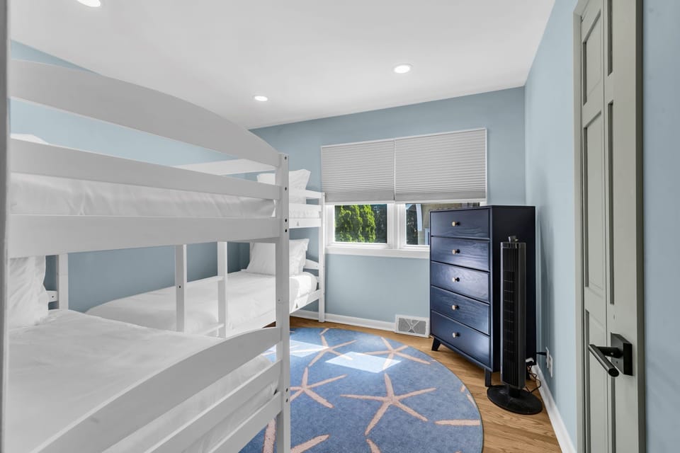 Bunk bedroom with twin-over-twin white bunks, navy five-drawer dresser, blue walls, and starfish round rug; sleeps two kids easily.