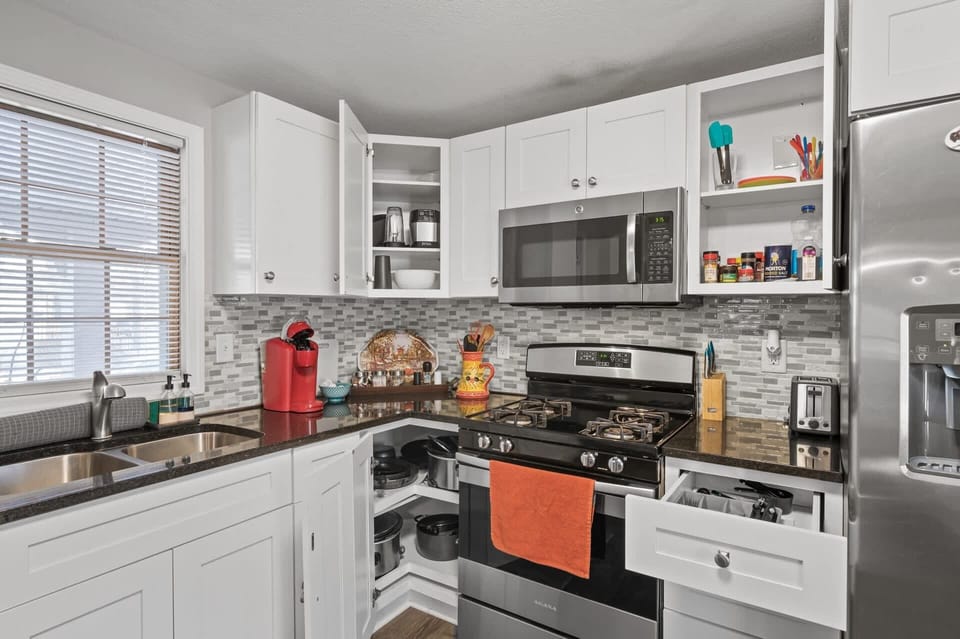 Bright corner kitchen w/ white cabinets, stainless appliances & a cheerful pop of color at the stove.