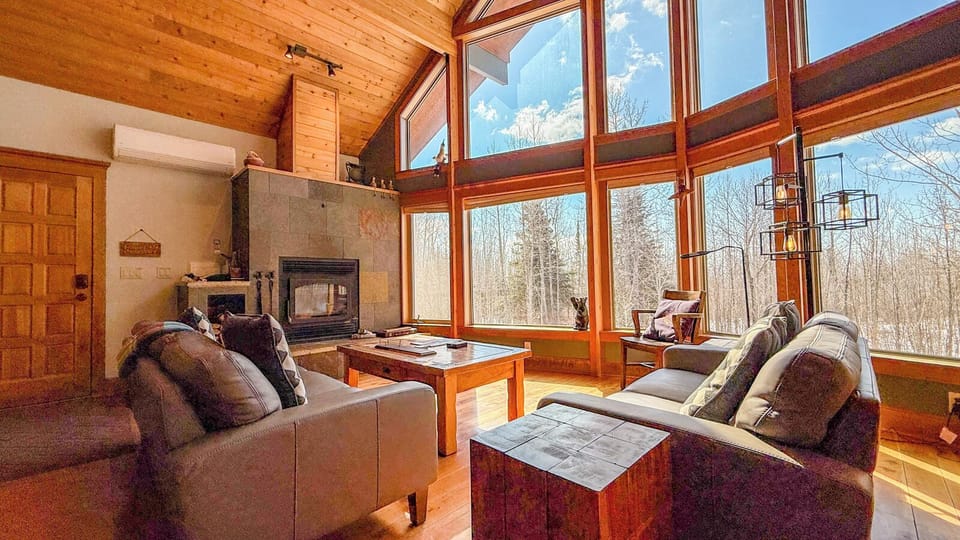 Unwind in your cozy living room where warm wood beams meet floor-to-ceiling windows, creating the perfect spot to relax by the fireplace.