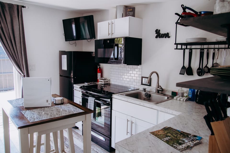 This full view of the kitchenette highlights its modern efficiency, featuring sleek white cabinetry, a marble-style countertop, and a black electric range.