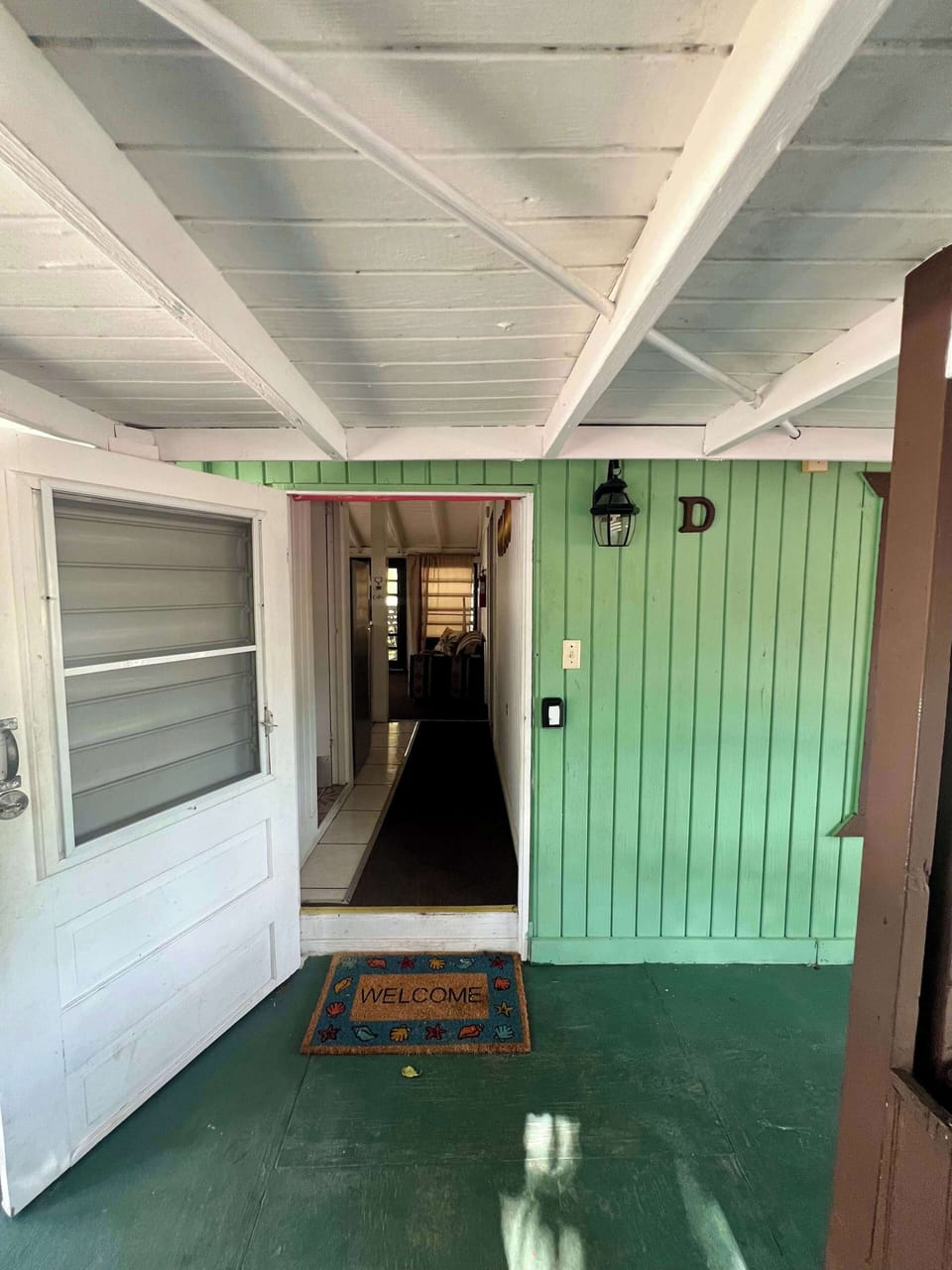 Charming cottage entrance with green wood paneling and welcome mat.

