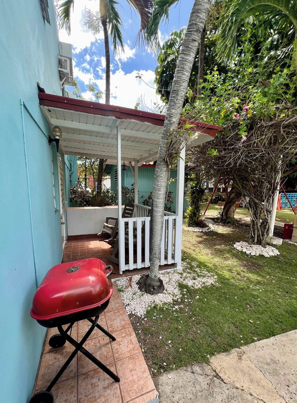 Side patio with charcoal grill, lush greenery, and a covered seating area.
