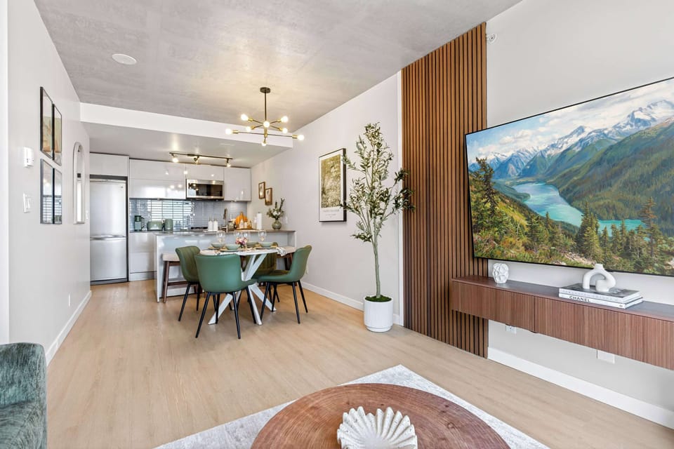 Spacious open-concept apartment design viewing from the living room into a modern kitchen with white cabinetry, stainless steel appliances, and an elegant dining space with modern lighting.