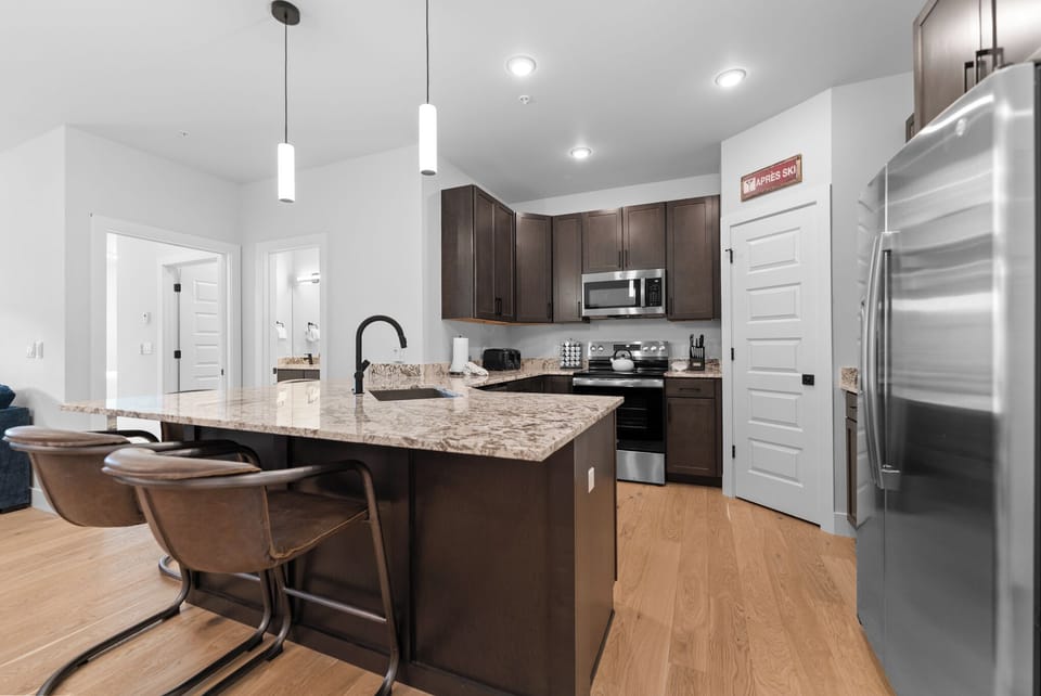 Full kitchen with stainless steel appliances, and a breakfast bar with seating for four.