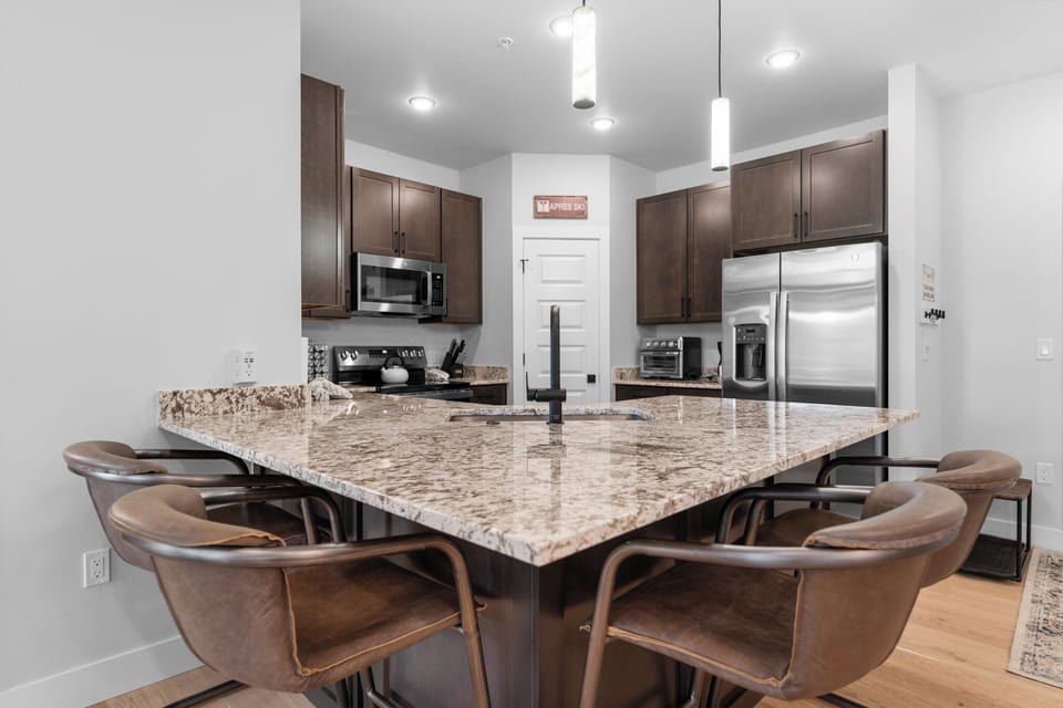 Full kitchen with stainless steel appliances, and a breakfast bar with seating for four.