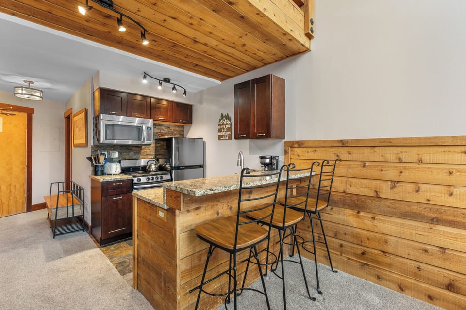 Full kitchen with stainless steel appliances and breakfast bar with seating for three.
