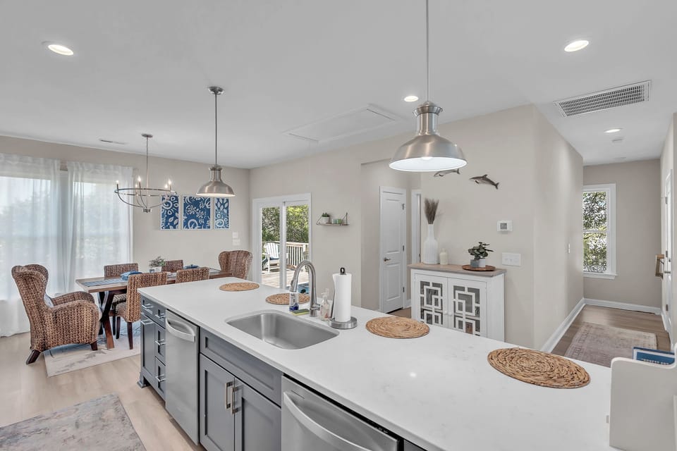 Your gourmet kitchen island invites culinary adventures with sleek countertops and coastal charm flowing into the bright dining space.