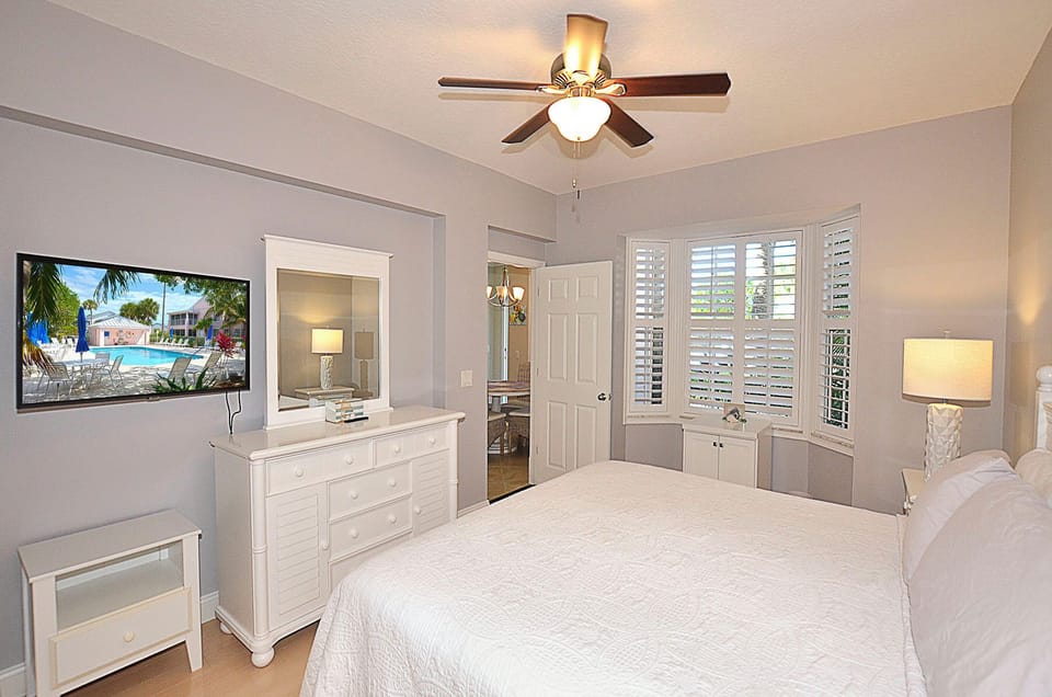 Peaceful Main bedroom sanctuary, complete with ceiling fan,  wall-mounted TV, and plantation shutters filtering gentle sunlight.