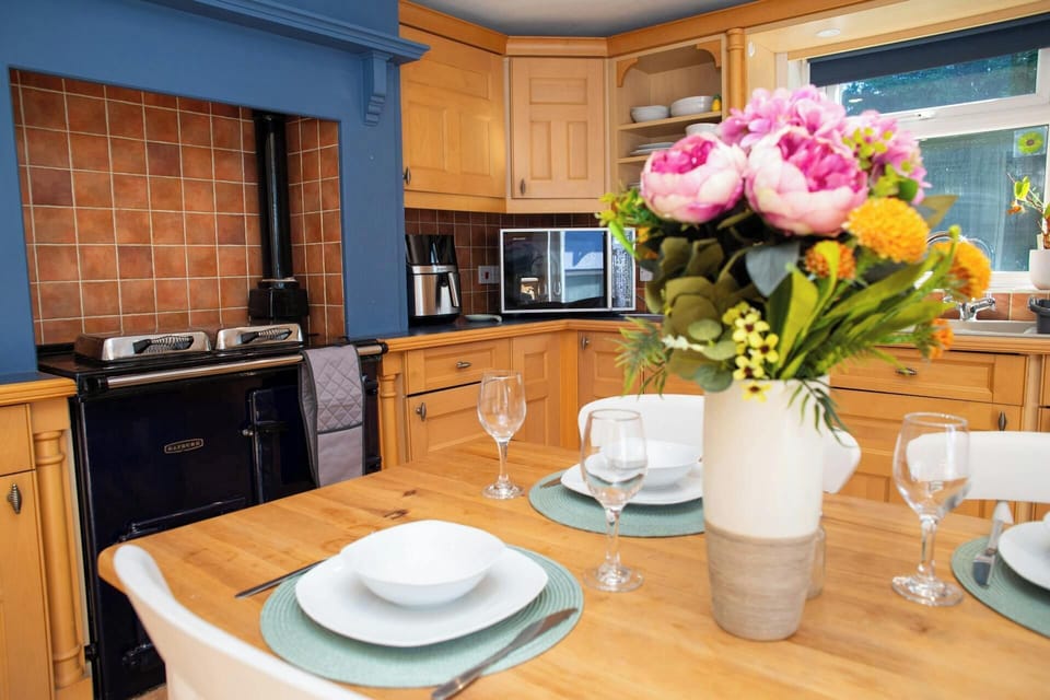 Wooden kitchen table set with plates and glasses, vase of flowers in foreground