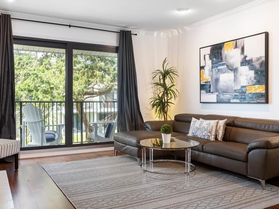 Leather sectional faces a round glass coffee table on a patterned area rug by sliding doors to a balcony.