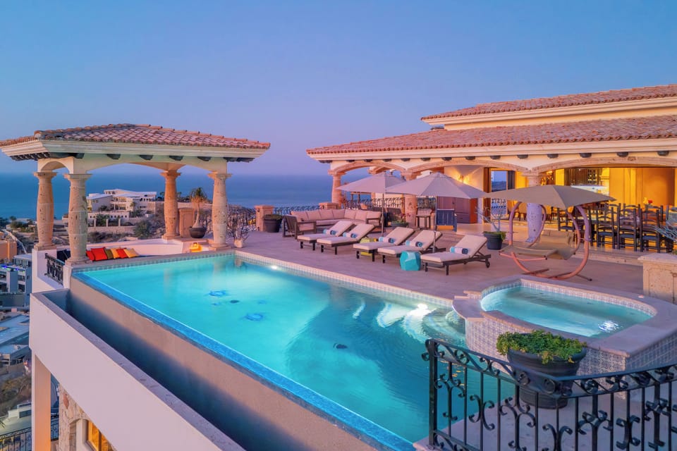 Stunning rooftop terrace with infinity pool, hot tub, and panoramic ocean views at dusk.