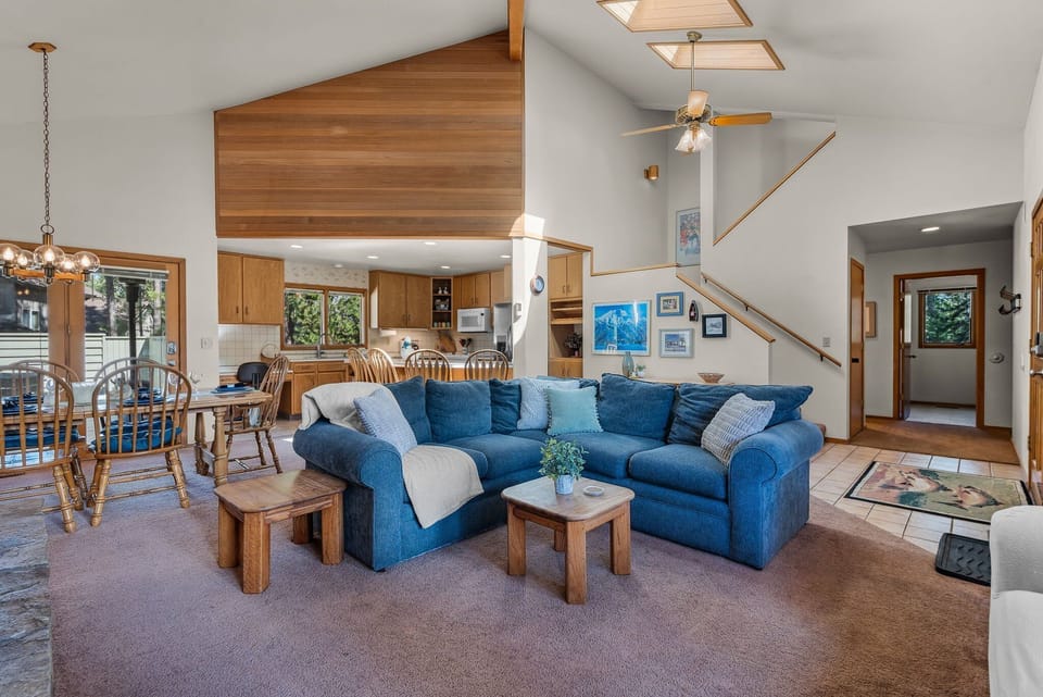 Relax in your spacious living area featuring a plush blue sectional sofa, warm wood accents, and vaulted ceilings with skylights that flood the space with natural light.