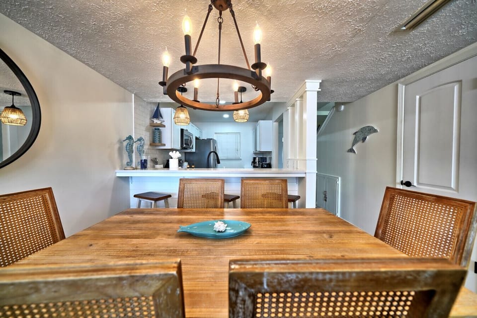 Discover your haven in this inviting dining area, featuring a rustic wooden table and stylish cane-back chairs. The open layout connects seamlessly to the modern kitchen, perfect for lively meals and beachside retreat gatherings.