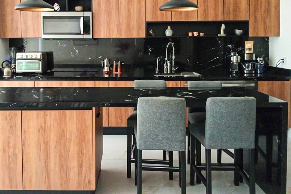 A sleek, extra-long black granite island serves as dining table, offering stylish, low-maintenance functionality and convenience for everyday meals or evening drinks.