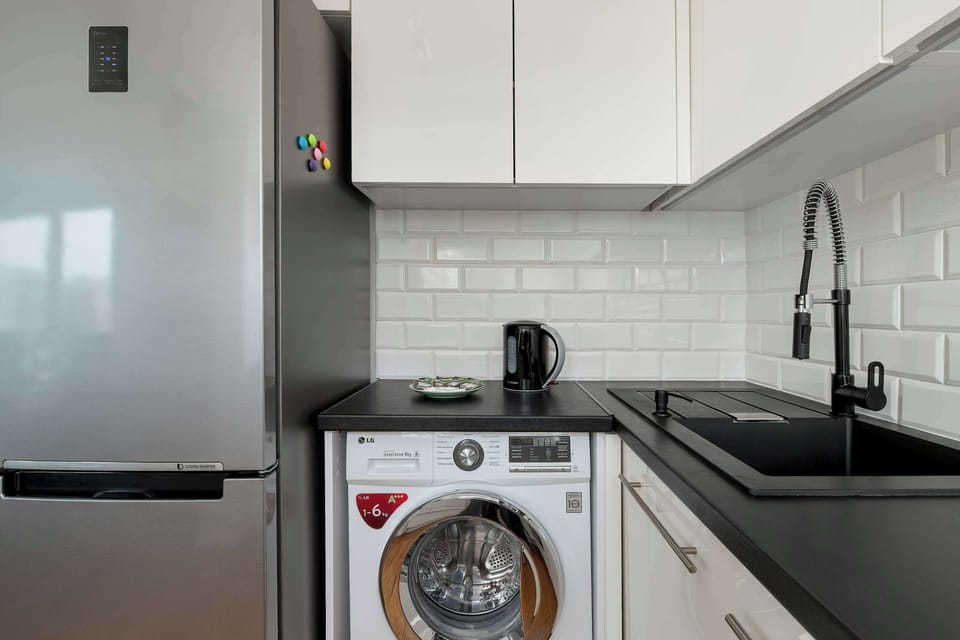 A compact kitchenette corner with white cabinets, a sink, and a washing machine. Clean design and practical layout.