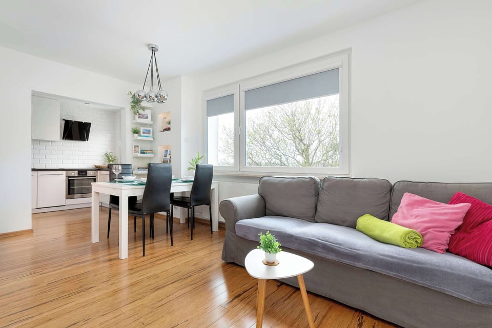 A wider view of the living space with a simple, open layout. Light tones and wooden floors keep it airy.