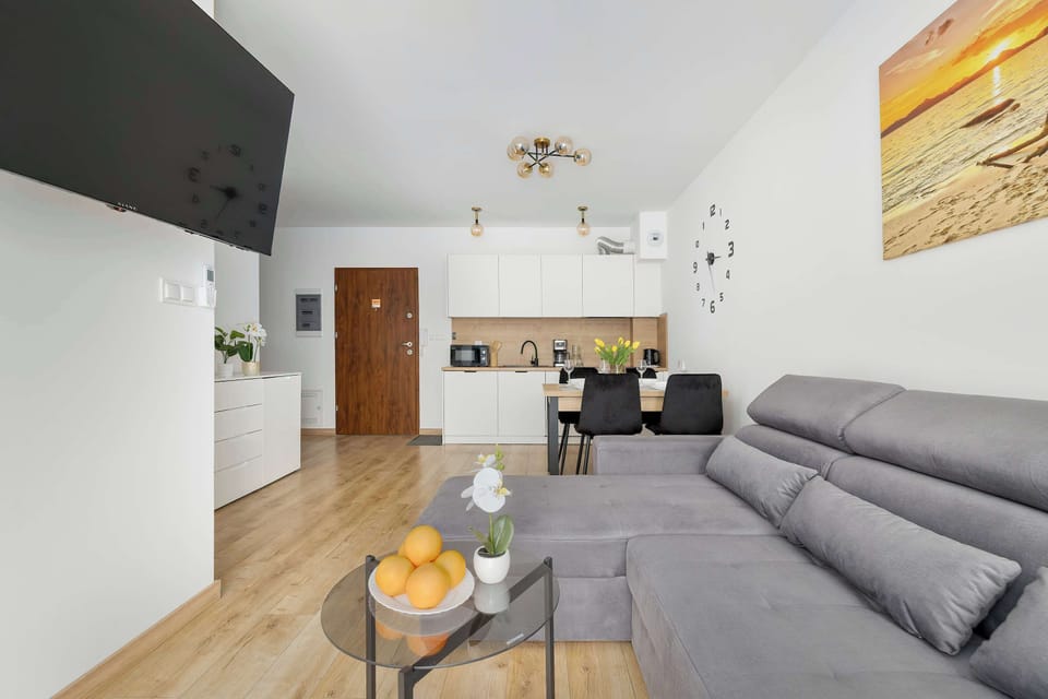 From this perspective, the entrance door is visible across from the living area and the dining setup. The layout is designed for efficient use of space, maintaining a bright and airy atmosphere.