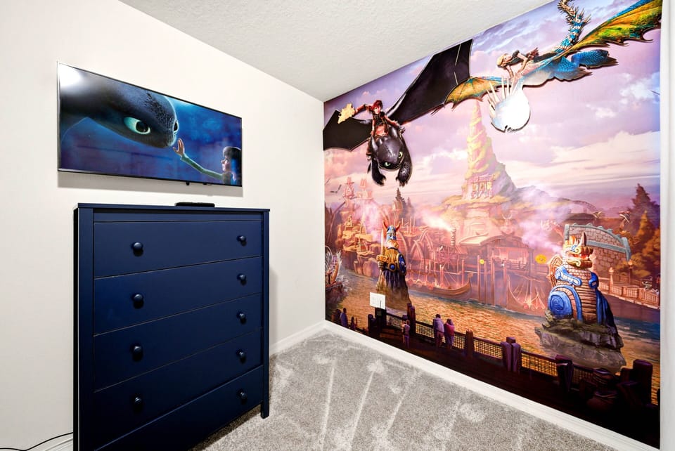 This lively children's room boasts an enchanting wall mural that inspires imagination, complemented by a stylish navy dresser and a wall-mounted TV for cozy movie nights, while the soft carpet provides comfort for playtime fun.