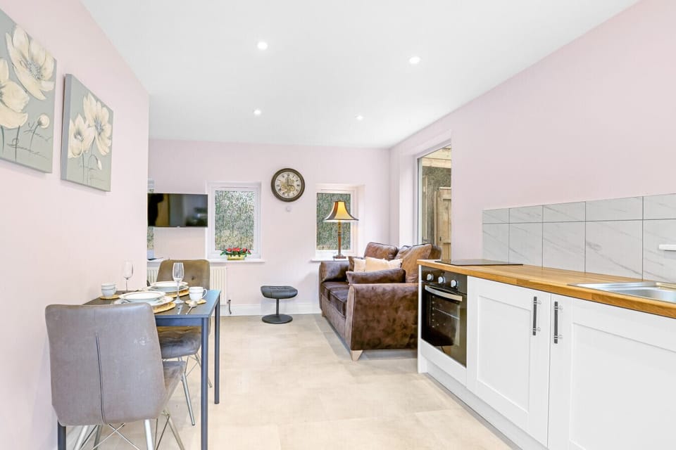 This compact open-plan living area combines a modern white kitchenette with a cosy dining nook and a brown leather sofa set against soft walls.