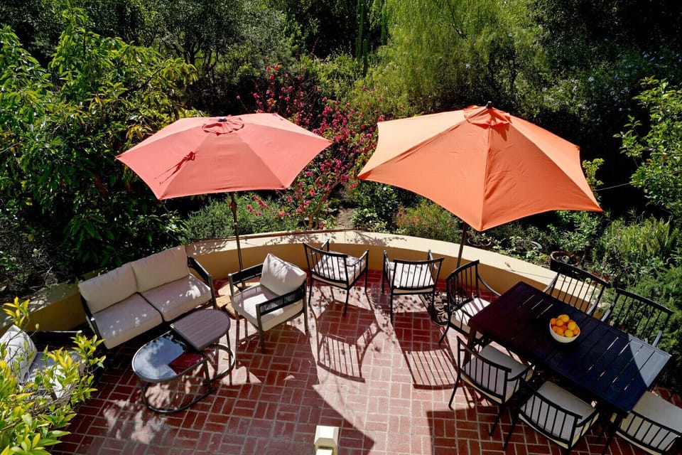 Lush, fully furnished garden patio with multiple seating zones and shade umbrellas — ideal for dining, lounging, or simply taking in the surroundings.
