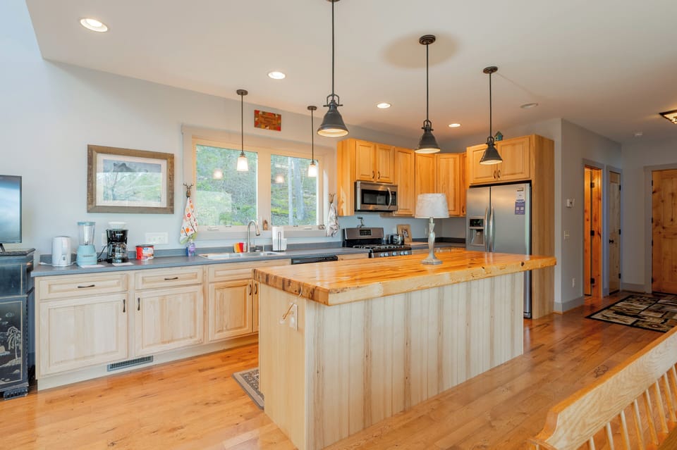 Cook in style in this modern, chef-ready kitchen featuring a massive wood island and stainless appliances. The open-concept flow leads to a cozy banquet dining area, perfect for family feasts with a view of the forest.