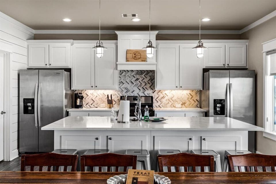 Fully equipped kitchen with white cabinetry, stainless steel appliances, and large island seating in Port Bolivar beach house
