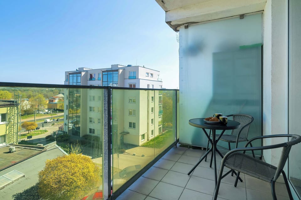 A balcony with glass railings offering a stunning view of the surrounding area, equipped with seating and a table for outdoor relaxation.