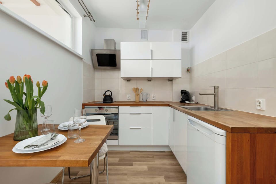 A wooden dining table is set with white plates and glasses, positioned neatly next to the kitchenette counter. A tall glass vase with tulips serves as a cheerful centerpiece for the meal setup.
