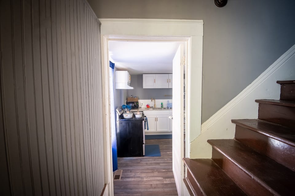 Just inside the entry, you’re welcomed into a cozy, functional layout with a glimpse into the kitchen. You’ll also notice a portion of the home’s original staircase—now closed off—a subtle reminder of the property’s history as a once full, single-family ho