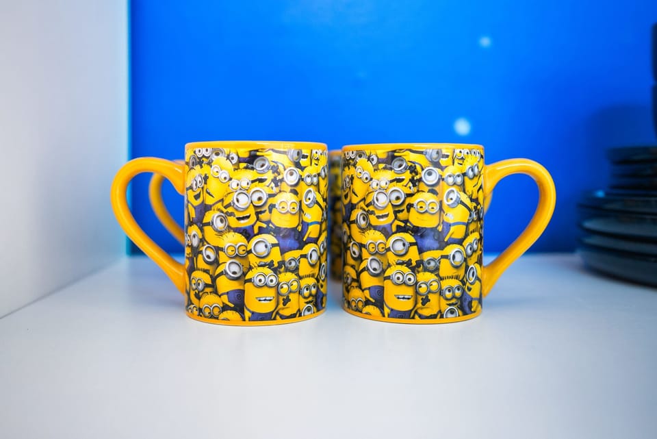 Two yellow mugs featuring minion characters against a blue background